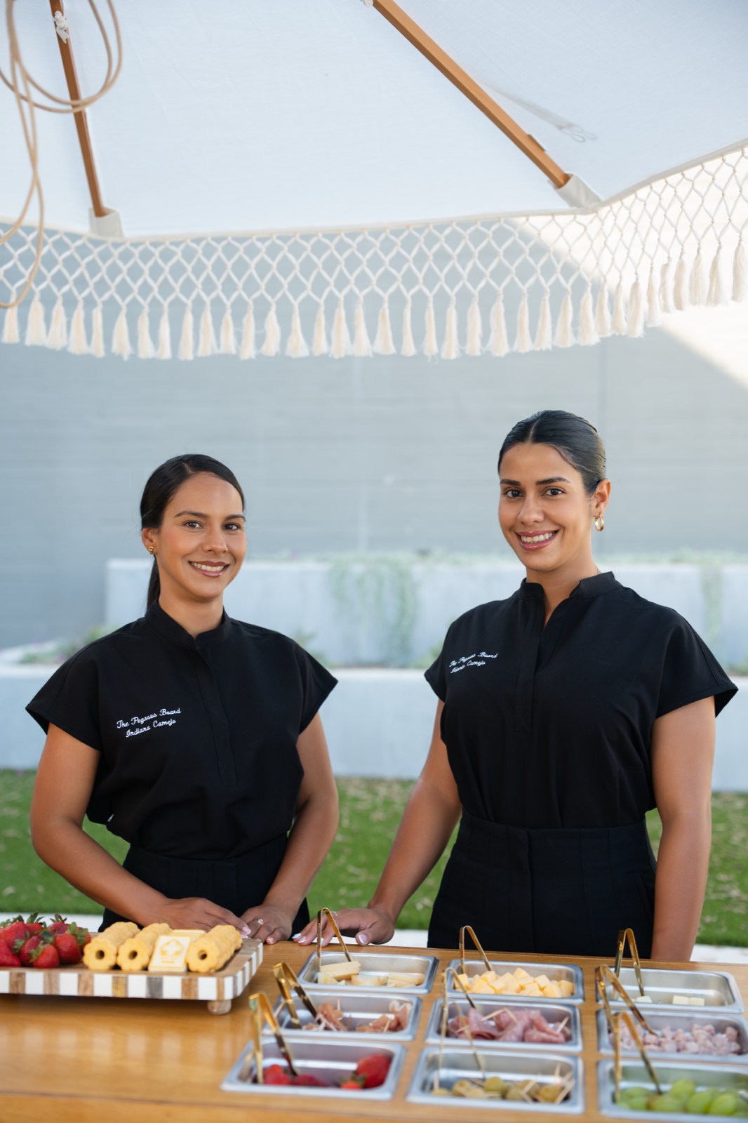 Dos anfitrionas uniformadas de The Pegasus Board detrás del buffet de charcutería